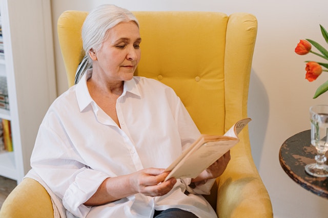 elderly woman reading a book in a chair 