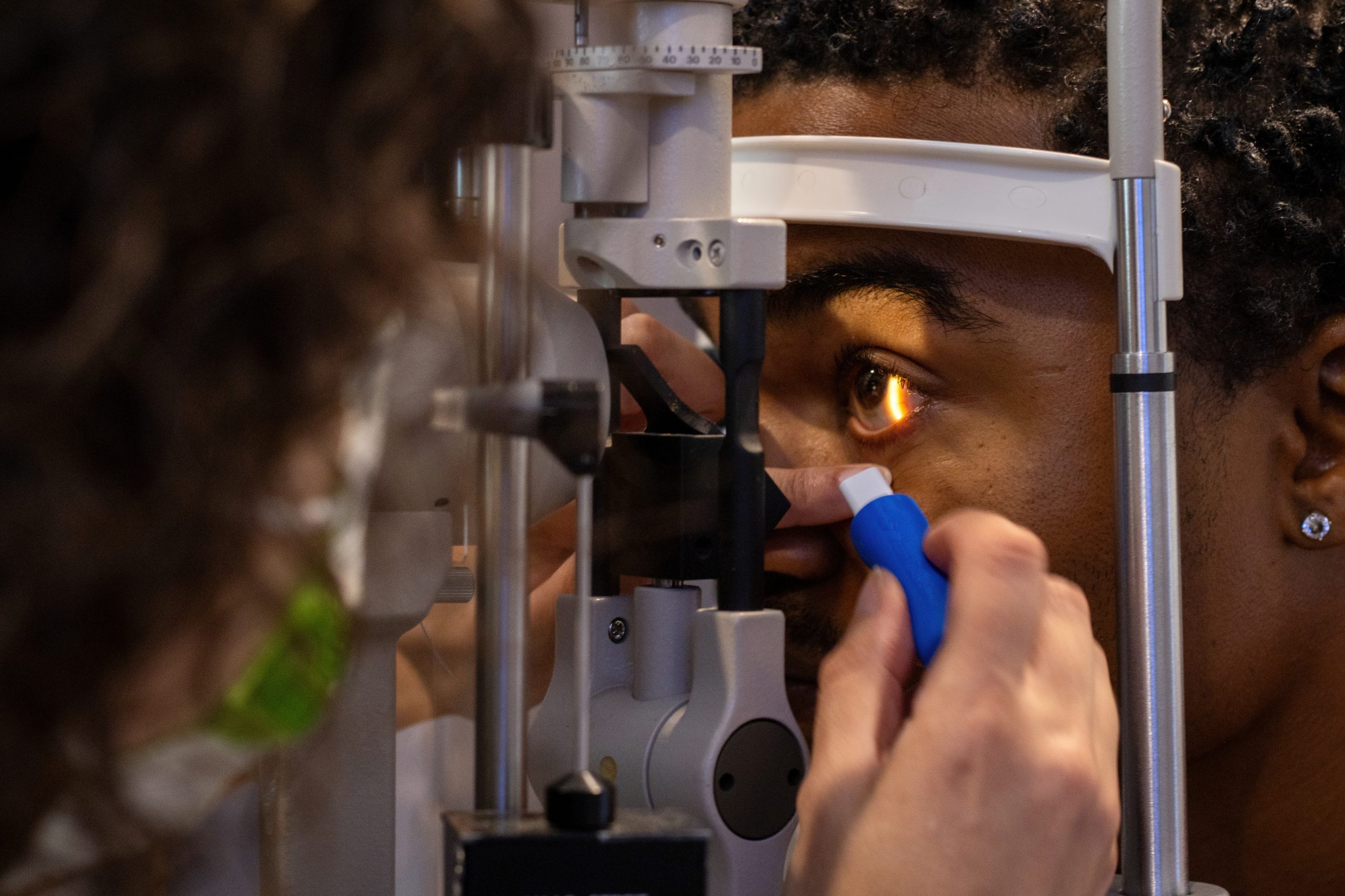 Image of woman during an eye exam. An eye doctor uses a tool to examine the patient’s open eye. Patient is leaning forward with her face inserted in eye care diagnostic equipment.