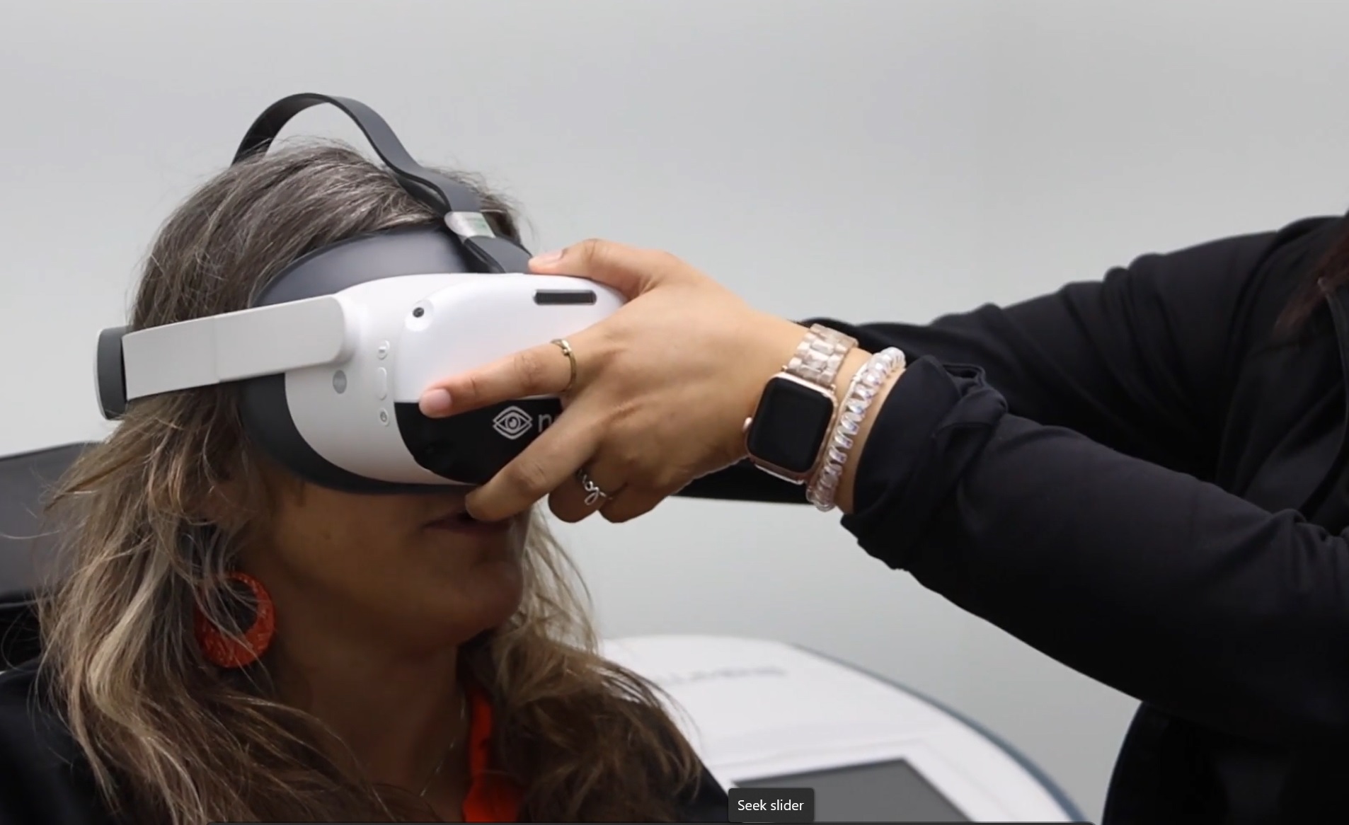  Image of seated woman wearing Neurolens headgear. An eye doctor’s hands are assisting with the placement of the Neurolens mask.