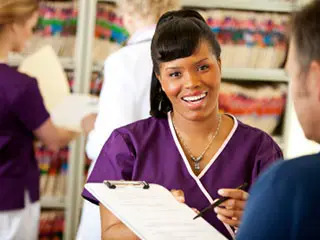Smiling nurse holds clipboard toward camera.